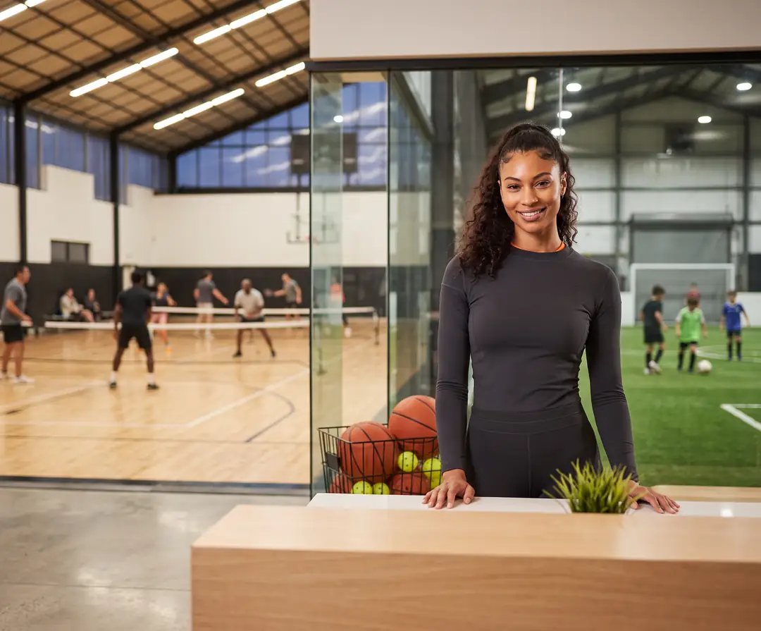 Facility director at the front desk of a busy sports facility during evening court bookings