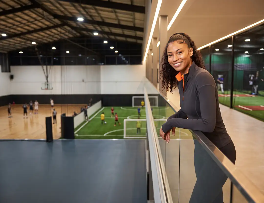 Facility director on the upper walkway of an indoor sports complex, with basketball, turf soccer and batting cages in use below