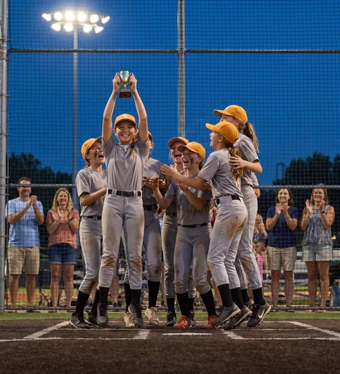 Youth softball team celebrating a championship trophy at home plate